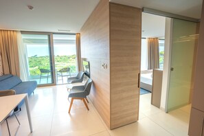 A modern hotel room with a sofa, chairs, a table, and a sliding door leading to a balcony with a view.