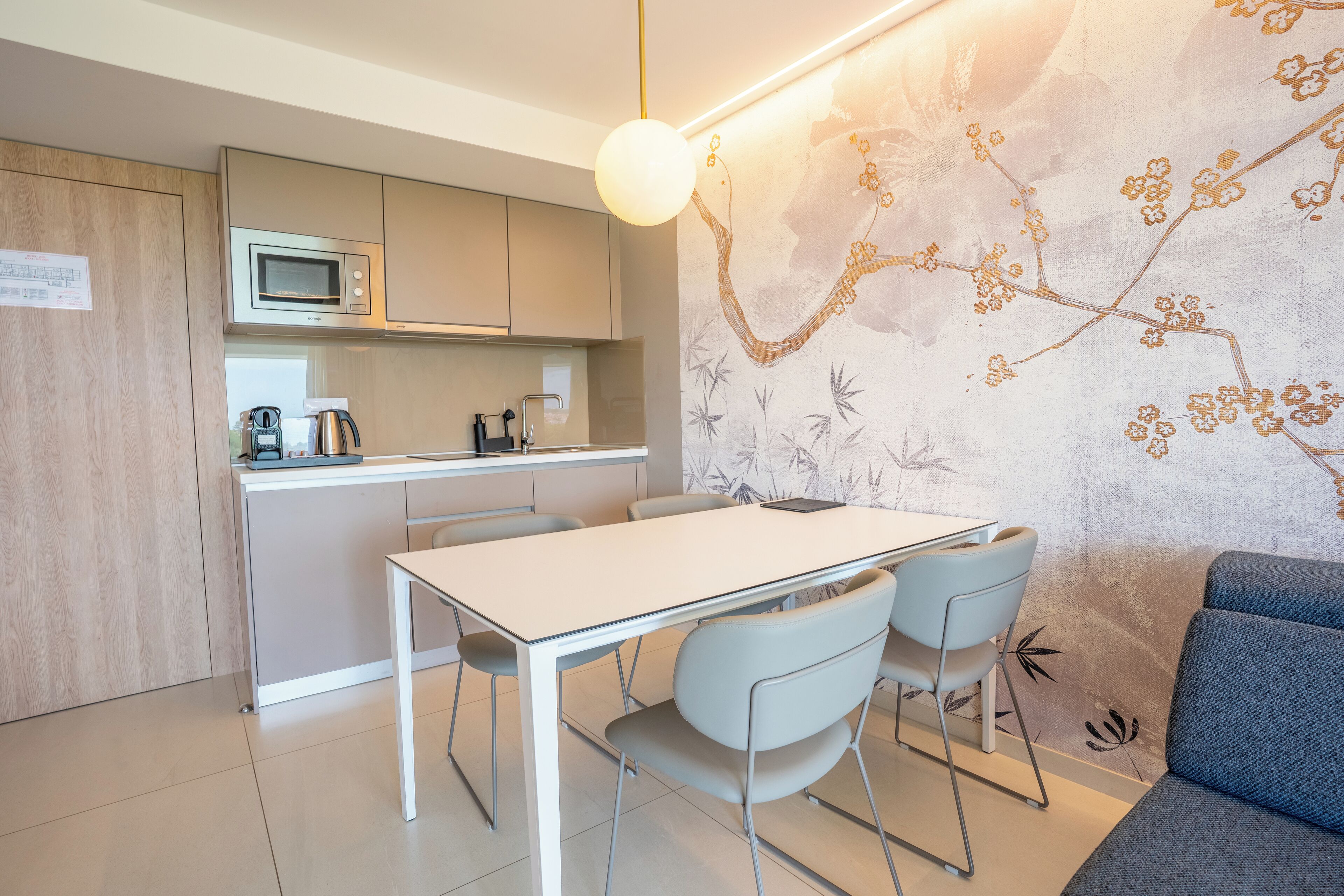 A modern kitchen with a microwave, kettle, and coffee machine. There is a dining table with chairs and a sofa in the living area.