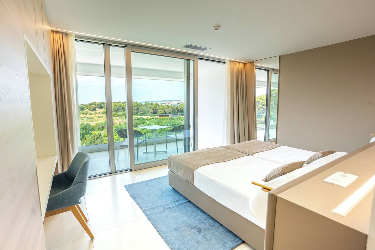 Una habitación de hotel moderna con una cama grande, un escritorio y vistas a un balcón con mesa y sillas.