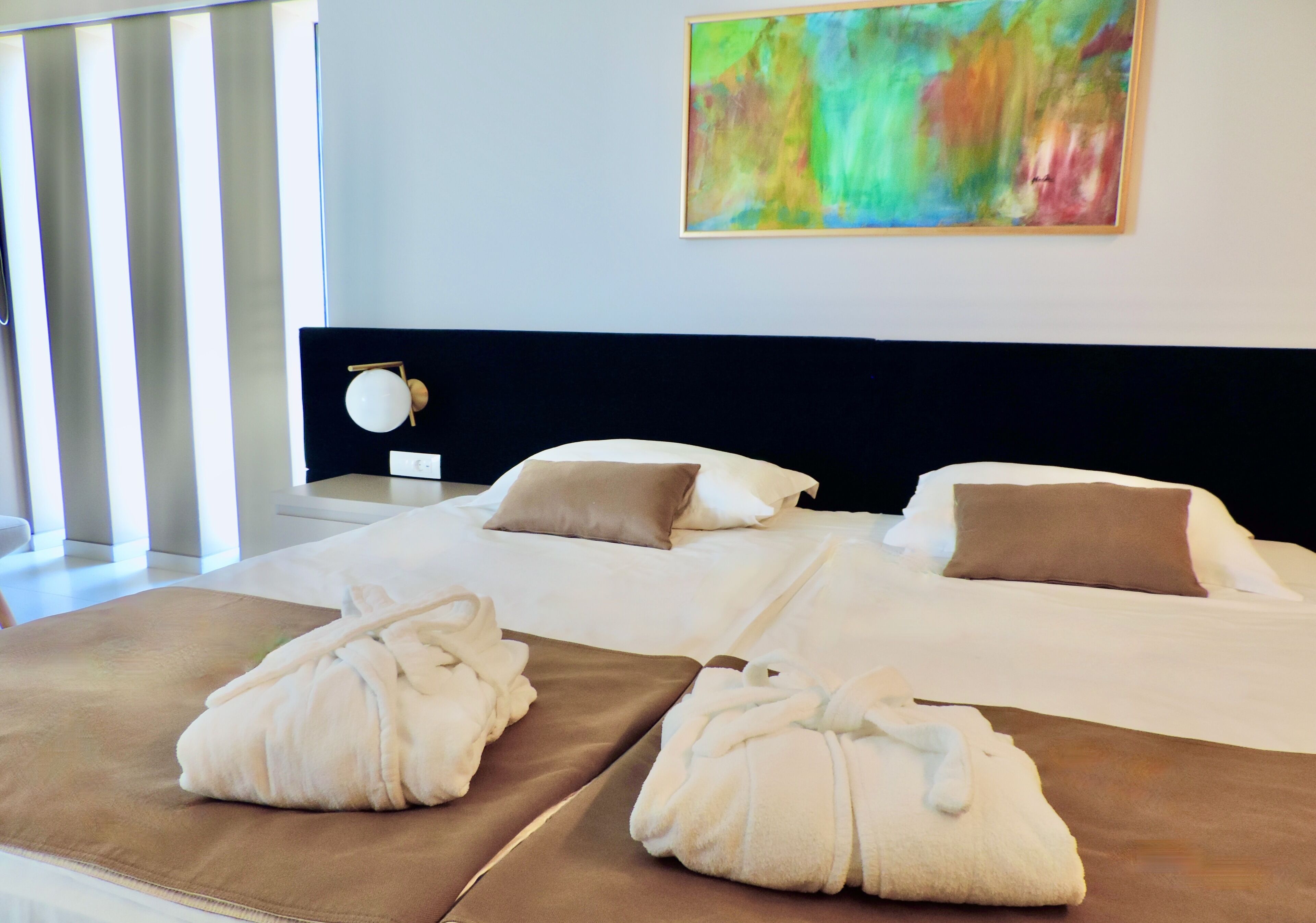 Une chambre d’hôtel avec deux lits, une grande peinture abstraite, une table de chevet avec une lampe et deux serviettes sur les lits.