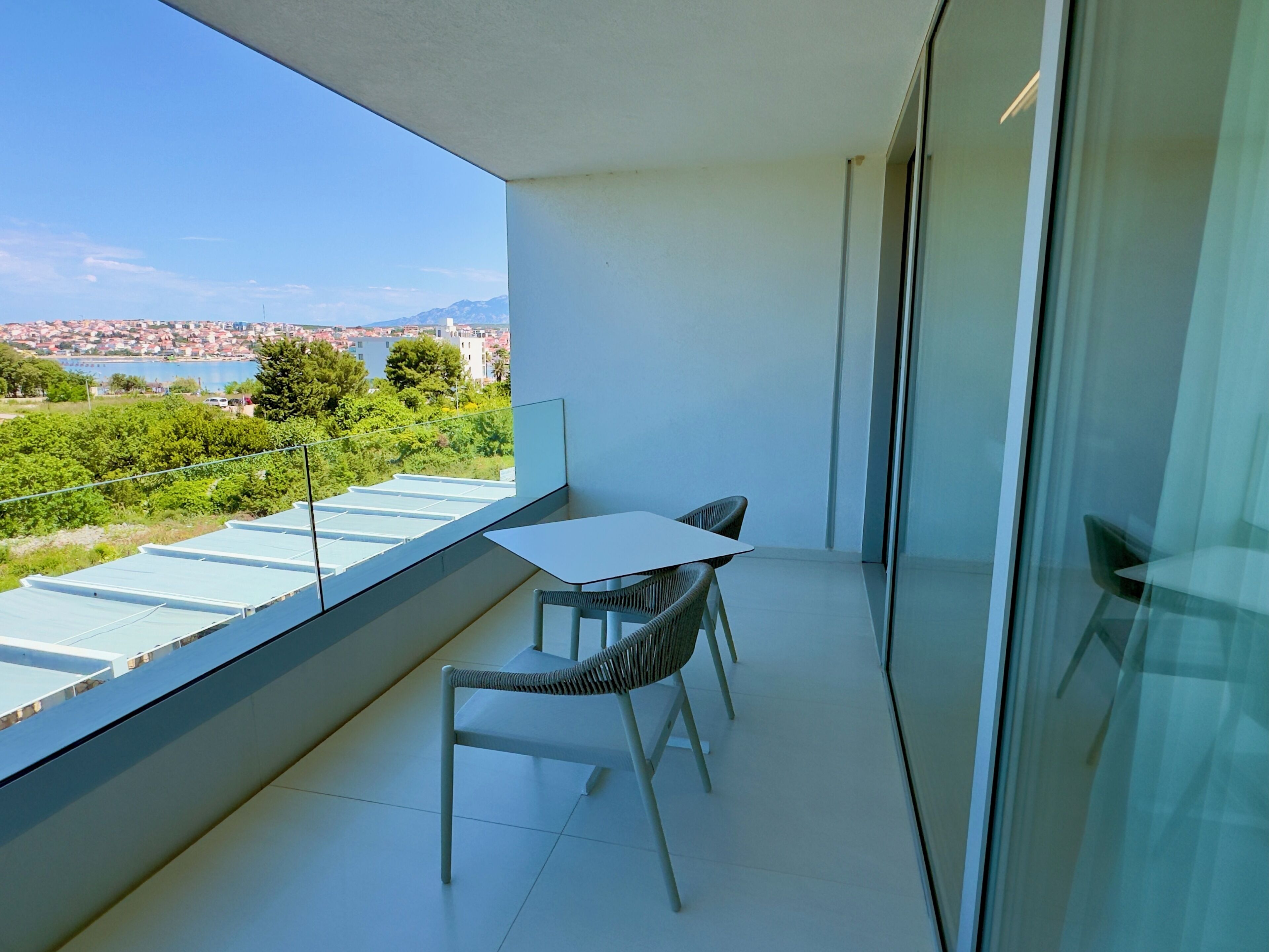 Ein Balkon mit Tisch und Stühlen, einer Glastür und Blick auf Stadt und Berge.