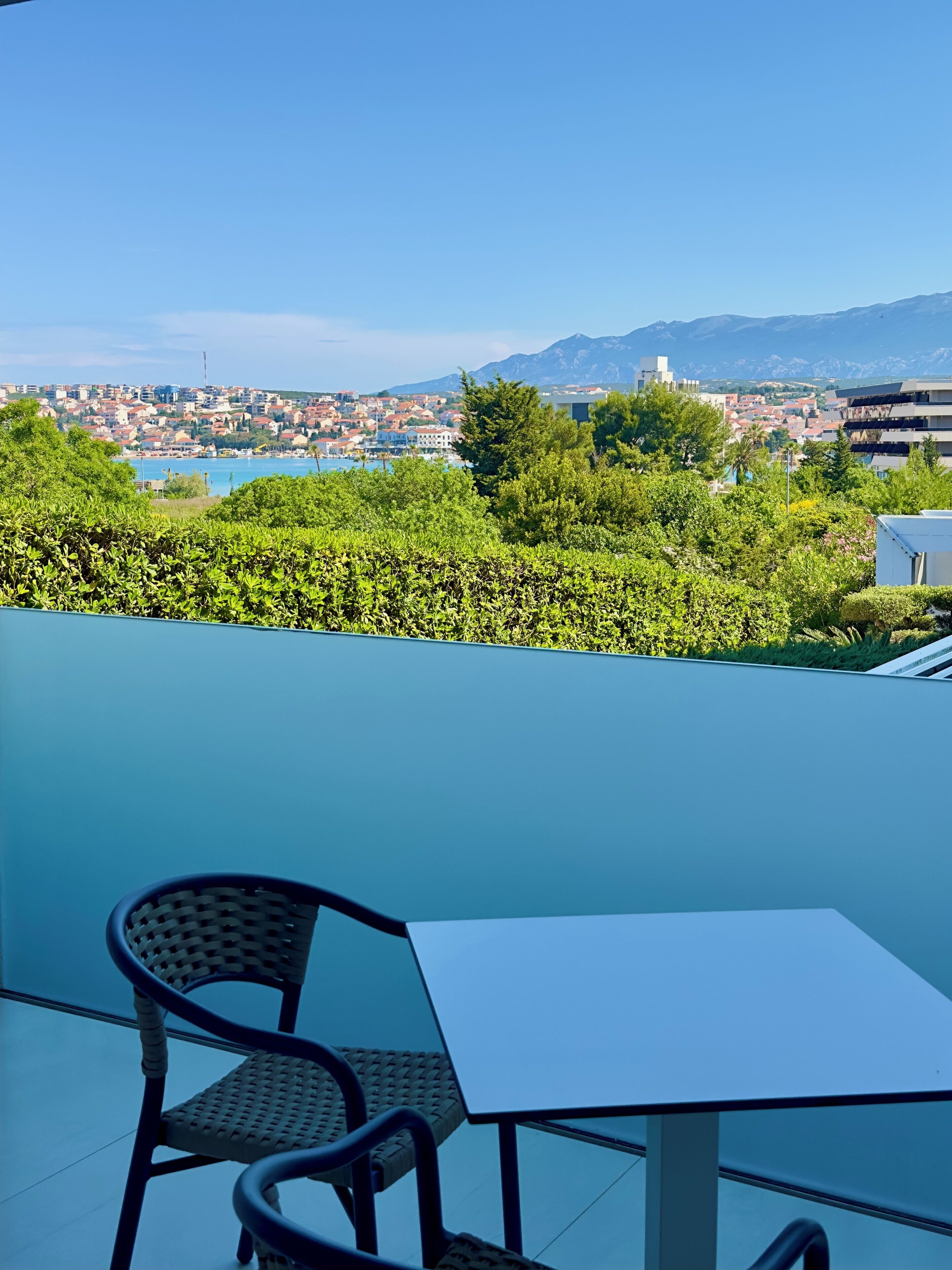 A terrace with a table and chairs, overlooking a cityscape with buildings and mountains.