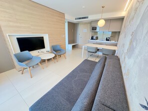 A modern living room with a sofa, two chairs, a TV, and a kitchen area with a microwave.