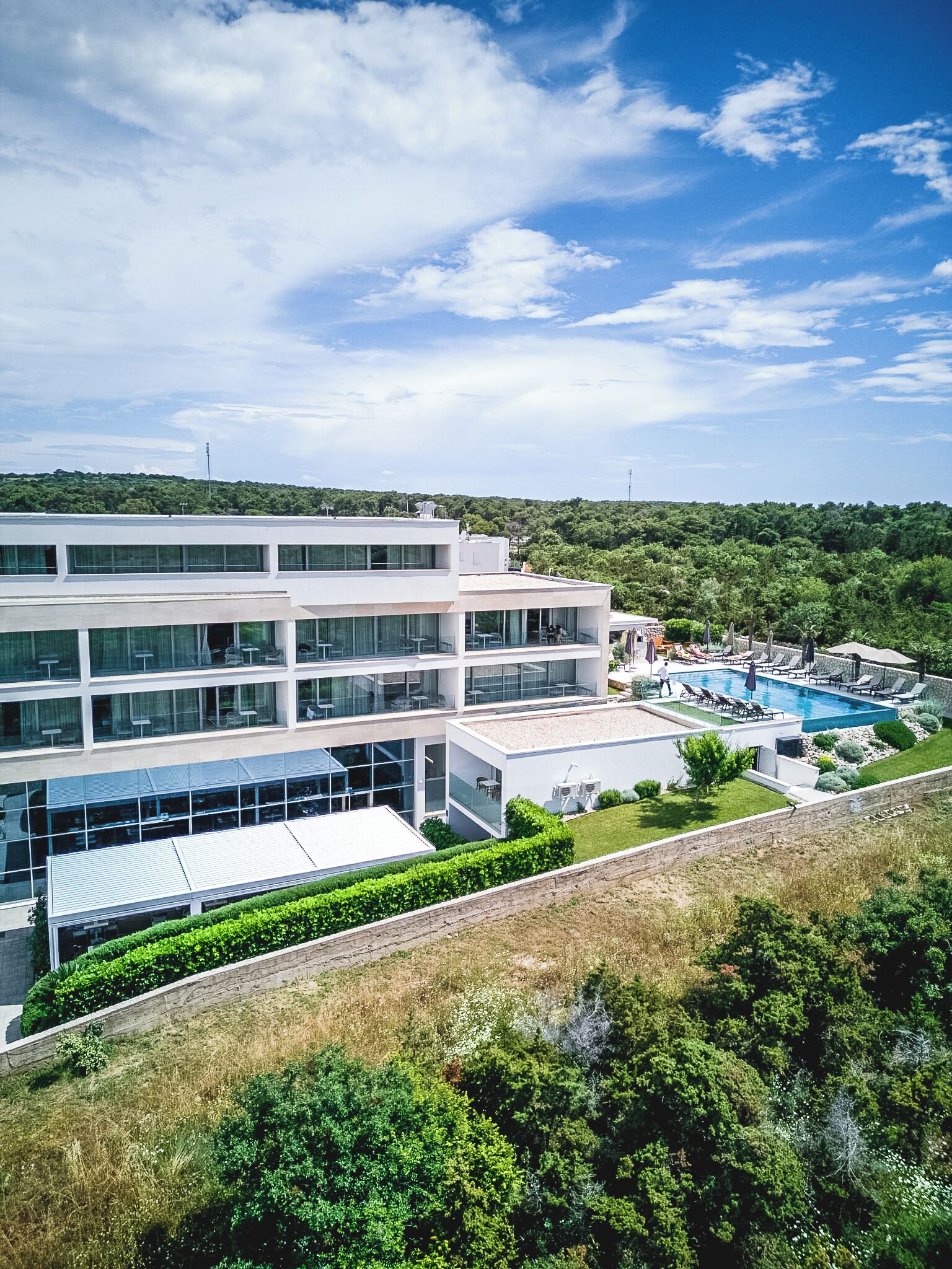 A modern building with multiple floors, a swimming pool, and a landscaped area with greenery.