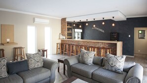 Uma sala de estar moderna com dois sofás cinzas, almofadas estampadas, uma mesa de centro e um bar com banquetas.