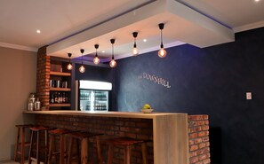 Un espace bar avec un mur bleu foncé, un mur en briques apparentes et un comptoir avec des tabourets.