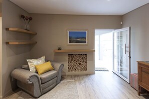 Un salon avec un canapé gris, une cheminée en bois et une porte vitrée donnant sur l’extérieur.