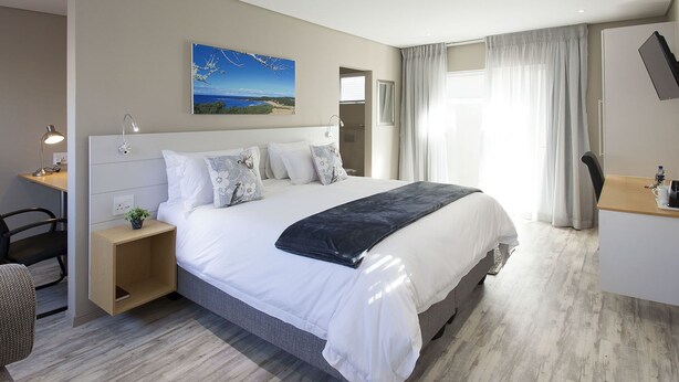 Quarto de hotel moderno com uma cama grande, uma escrivaninha, uma cadeira e vista para o mar.
