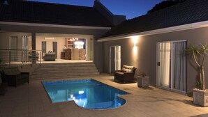 Uma casa moderna com piscina, área de bar e escada que leva à entrada.