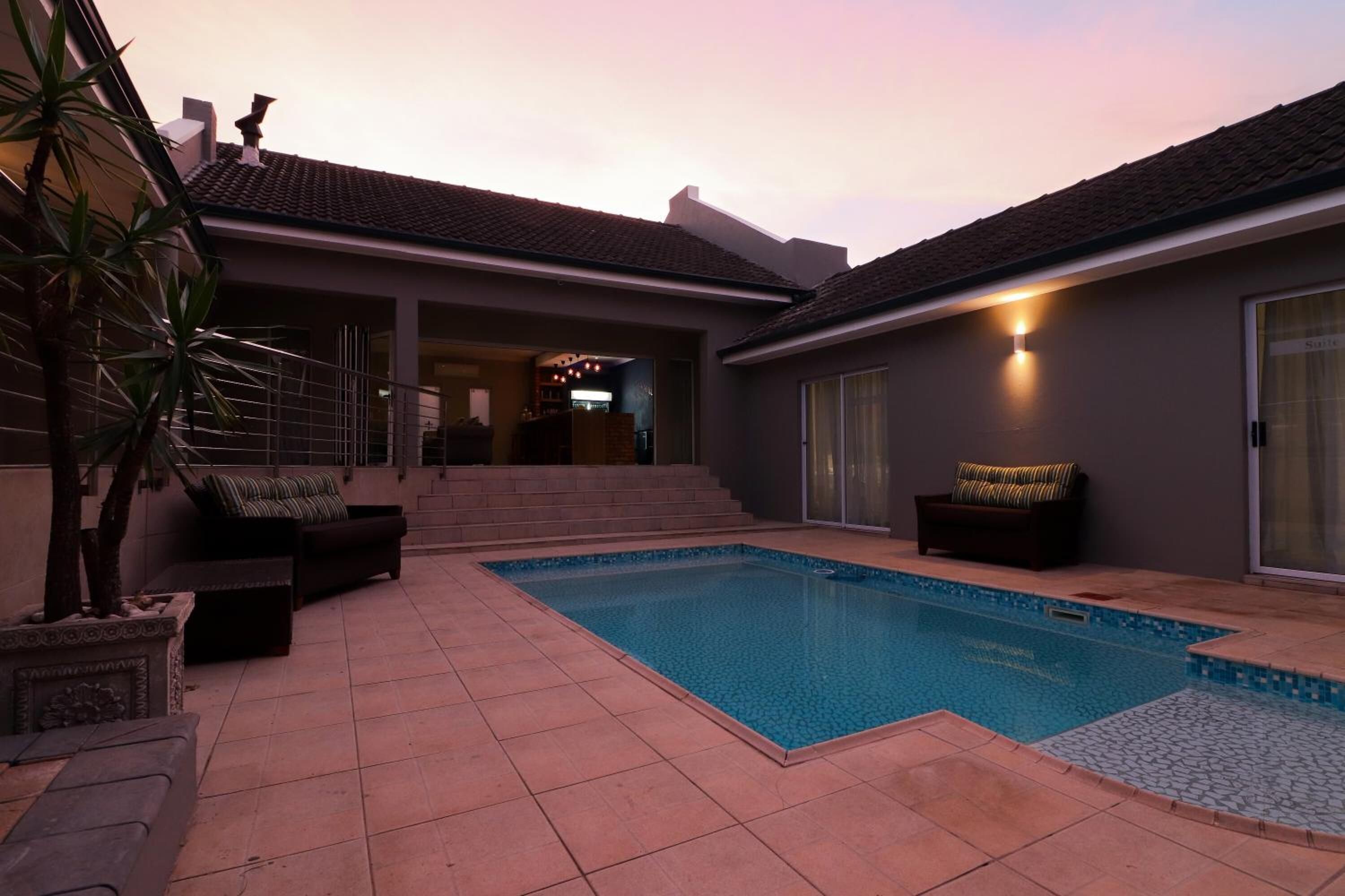 A swimming pool with a tiled deck, a covered patio area, and a staircase leading to an upper level.