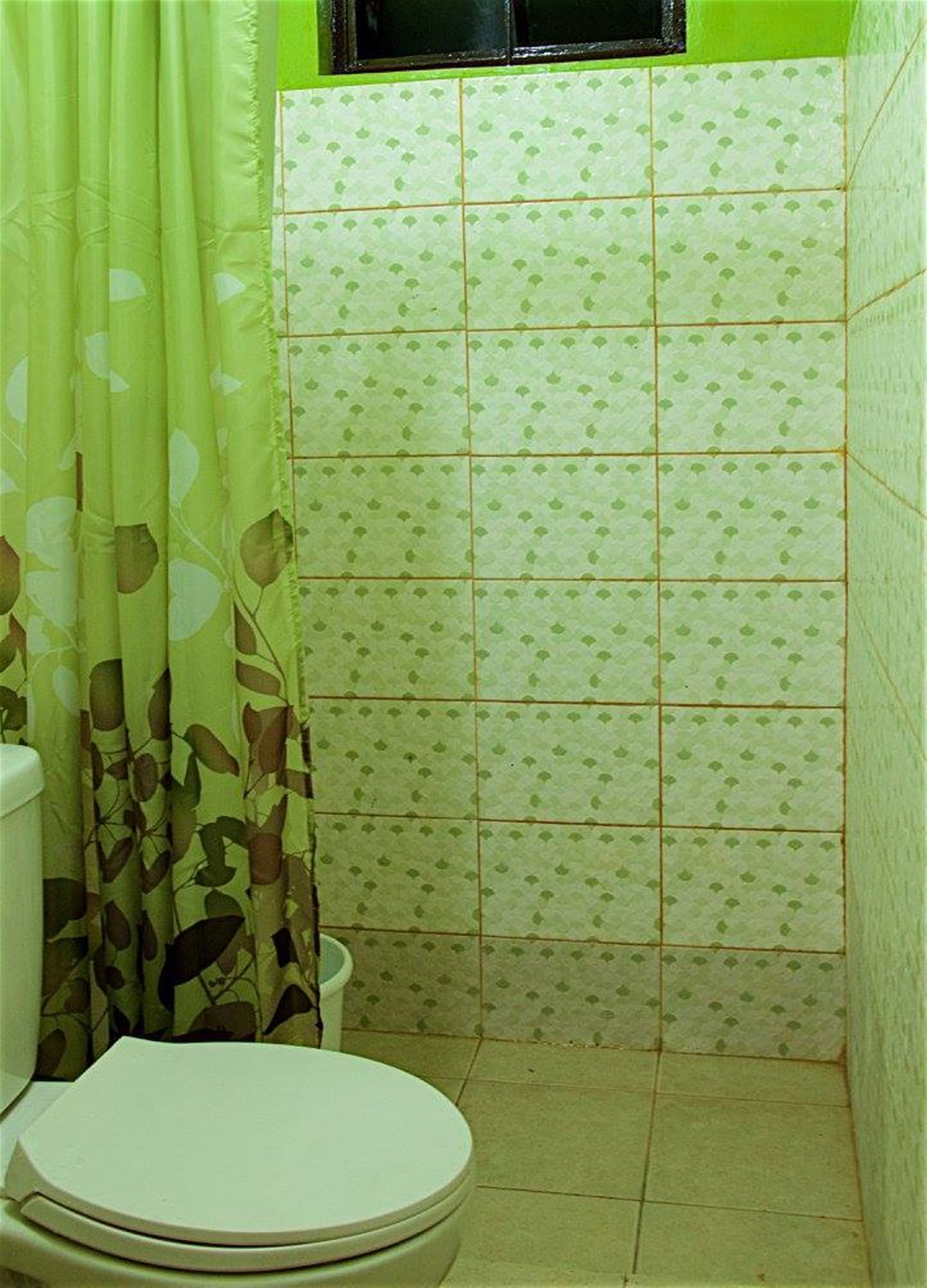 Un bagno con il water, una zona doccia con piastrelle a motivi floreali verdi e una tenda decorata con foglie.
