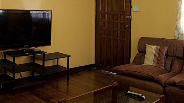 A living room with a flat-screen TV on a stand, a wooden door, and a brown sofa. - Sweet Star Transient Home (Baguio)