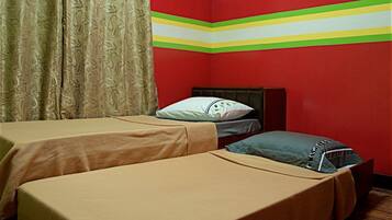A room with two single beds, a wooden headboard, a patterned curtain, and a red wall with a green and yellow stripe.