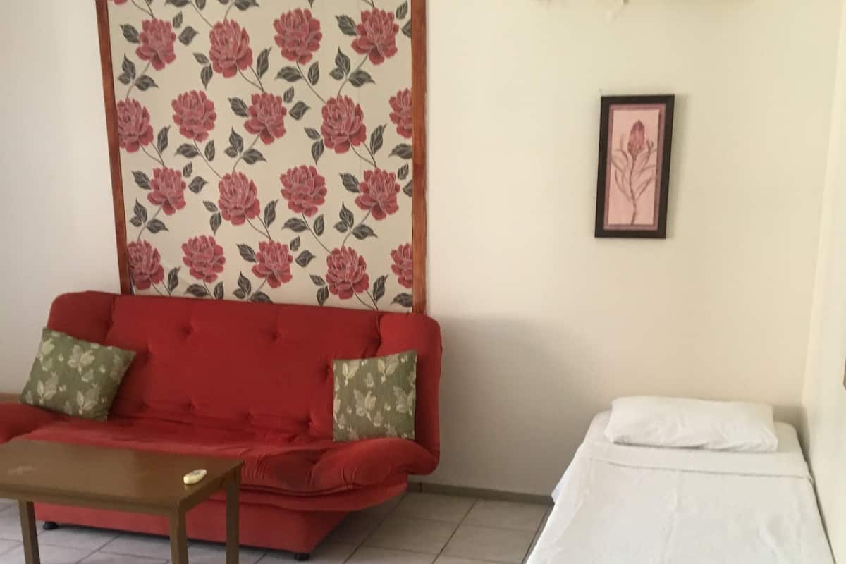 A room with a red sofa, a small wooden table, a white bed, a floral wallpaper, and a framed picture on the wall.