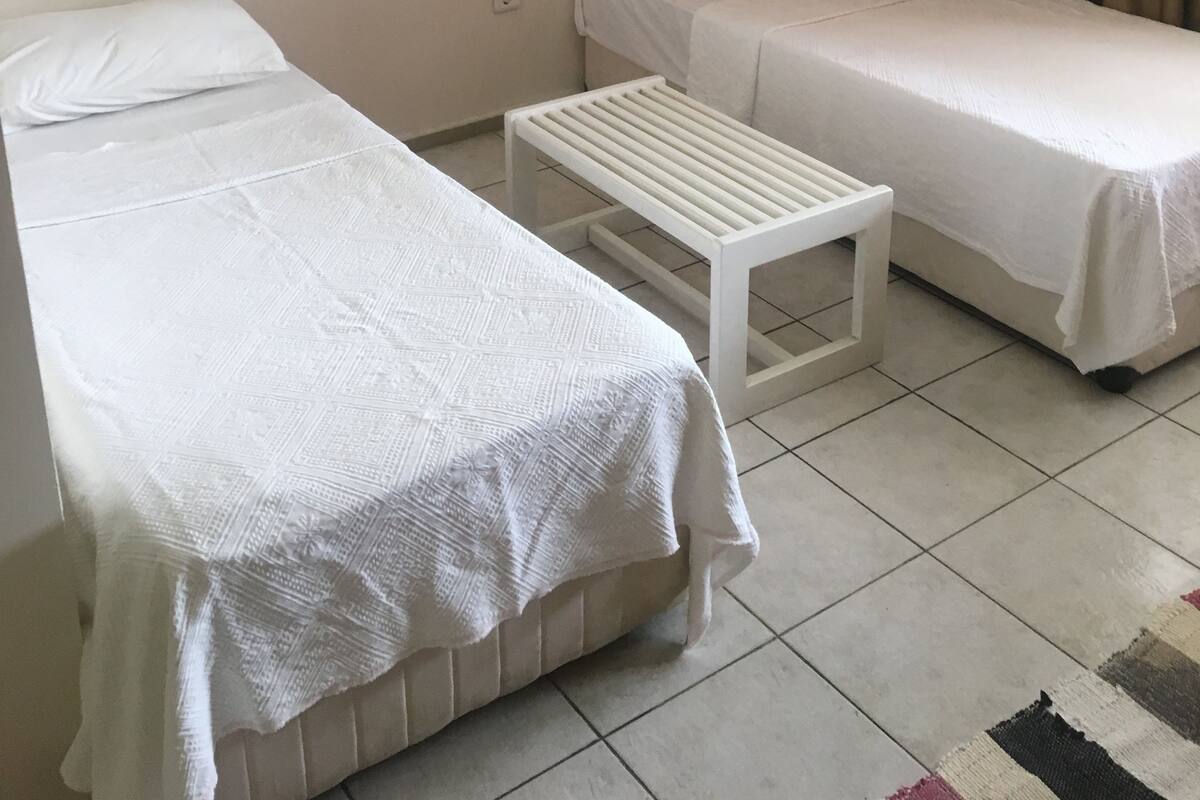A room with two single beds, a small table, a framed picture on the wall, and a curtain.
