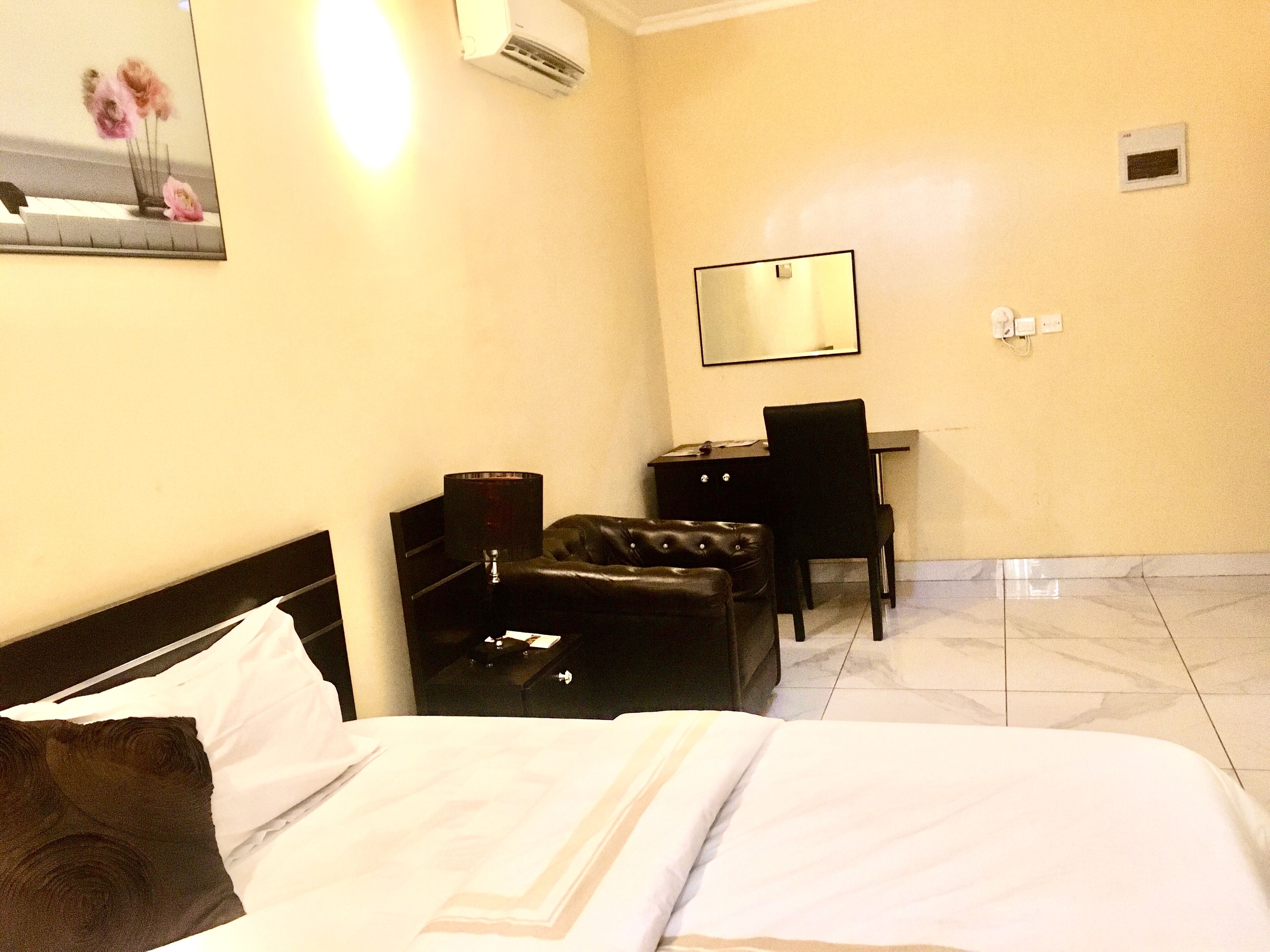 A hotel room with a bed, a desk, a chair, a lamp, and a mirror on the wall.