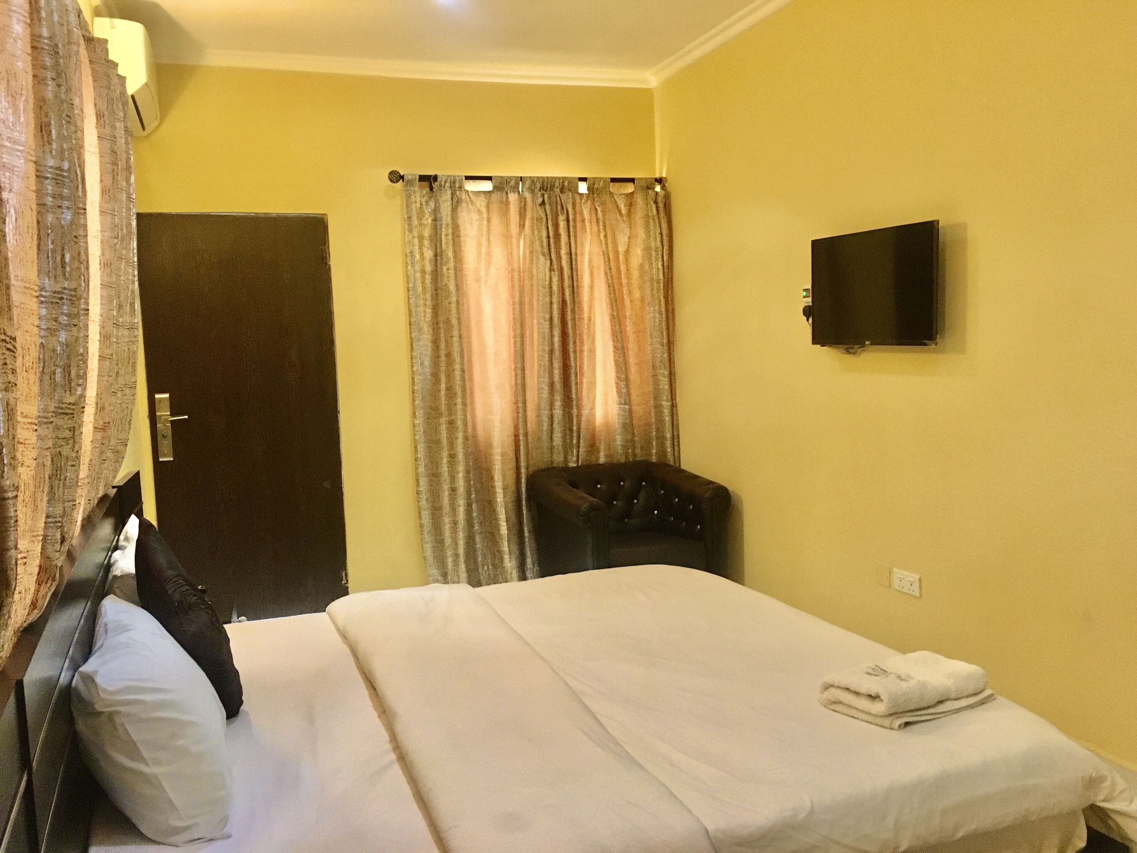 Una habitación de hotel con cama, una silla, televisor y cortina.