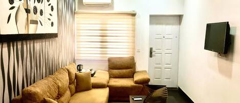 A living room with a sofa set, a coffee table, a decorative vase, and a flat-screen TV mounted on the wall.