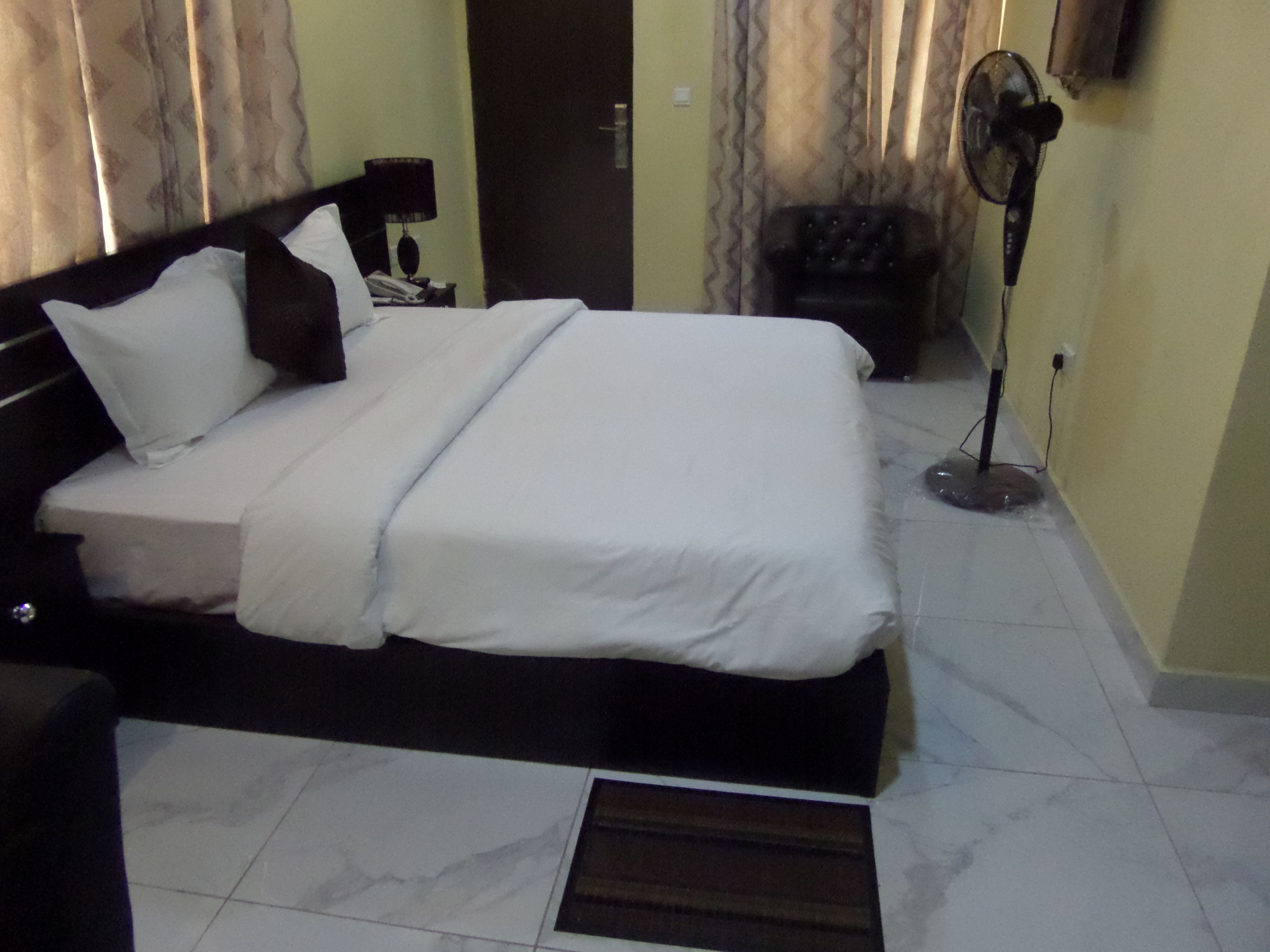 A neatly made bed with white linens, a black headboard, and a bedside table with a lamp.