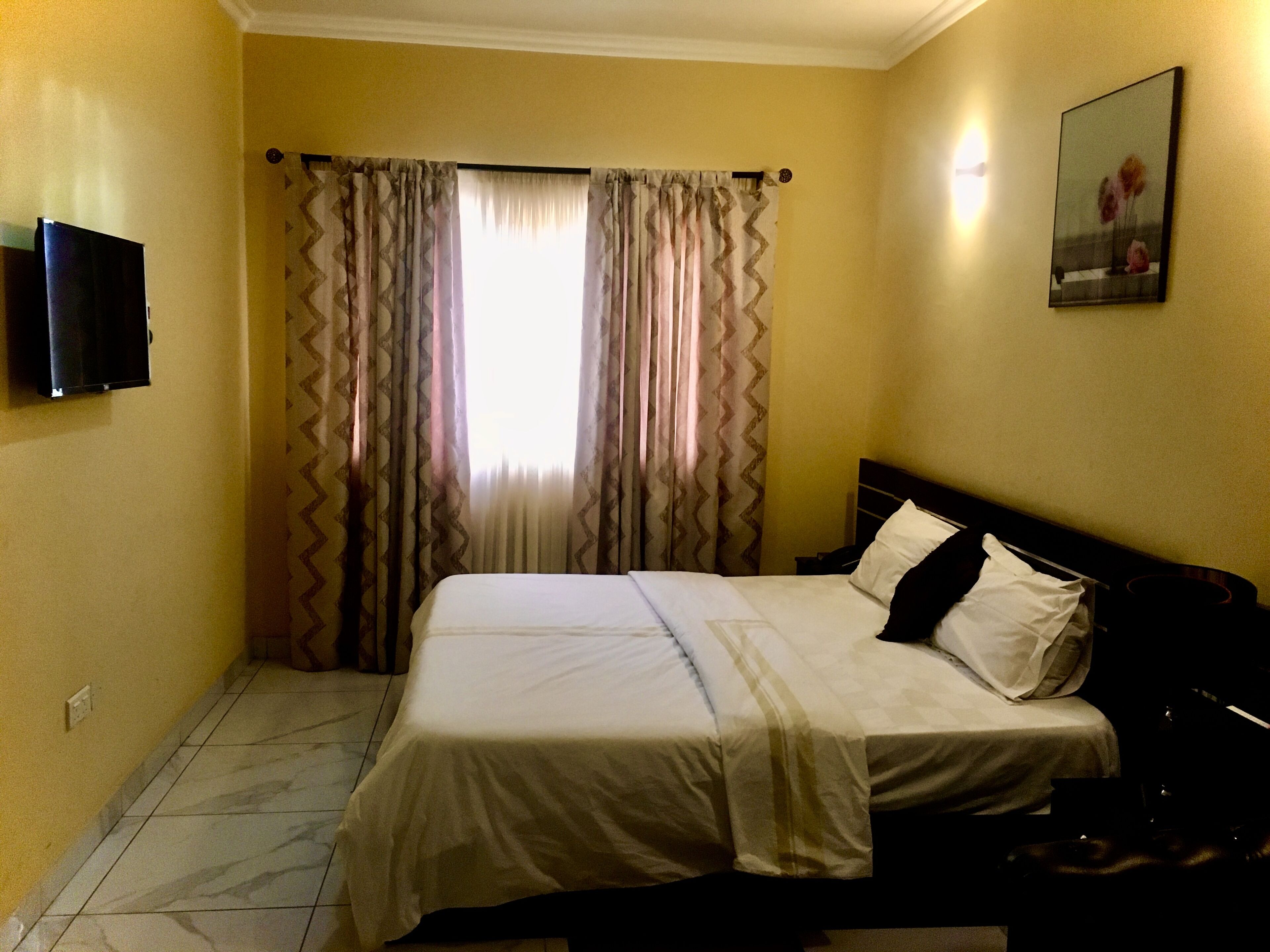 Habitación de hotel con cama, cortinas, televisor de pantalla plana y un cuadro en la pared.