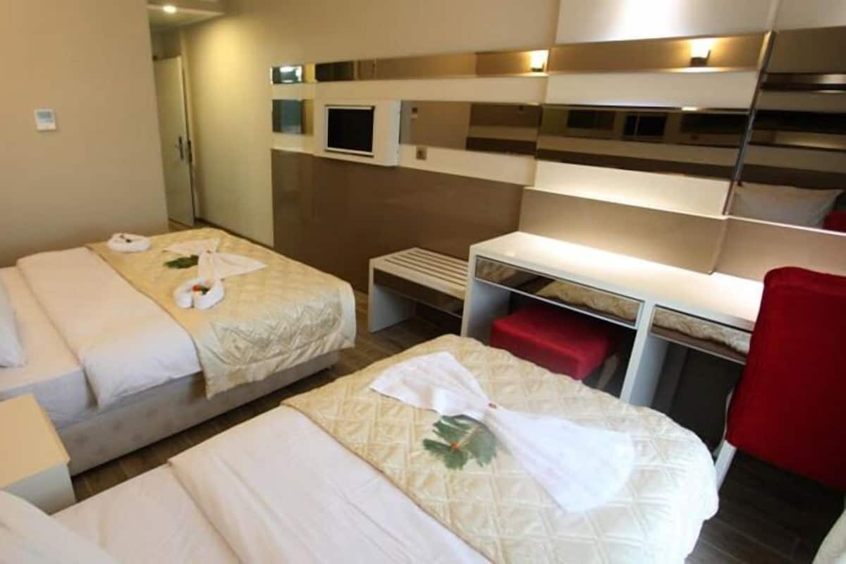 A hotel room with two beds, each with white linens and towels, a small desk, and a red chair.