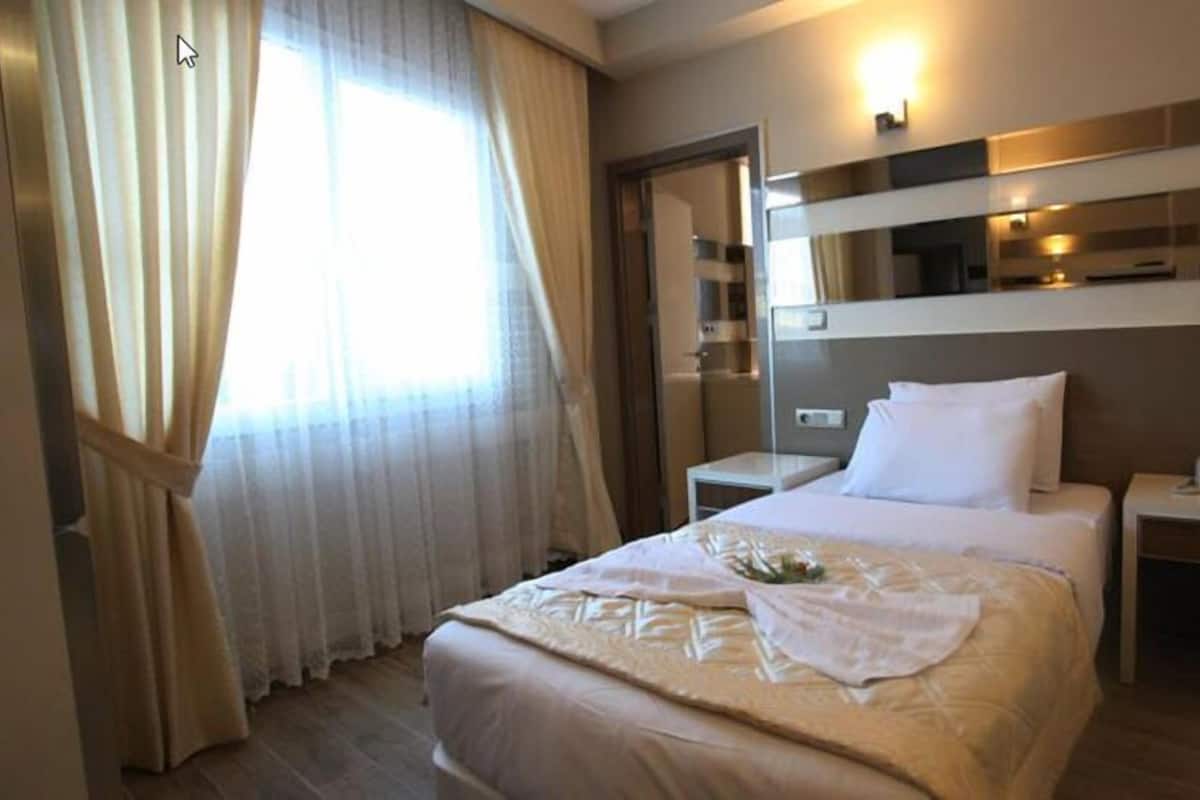A hotel room with a bed, bedside tables, a mirror, and a window with curtains.
