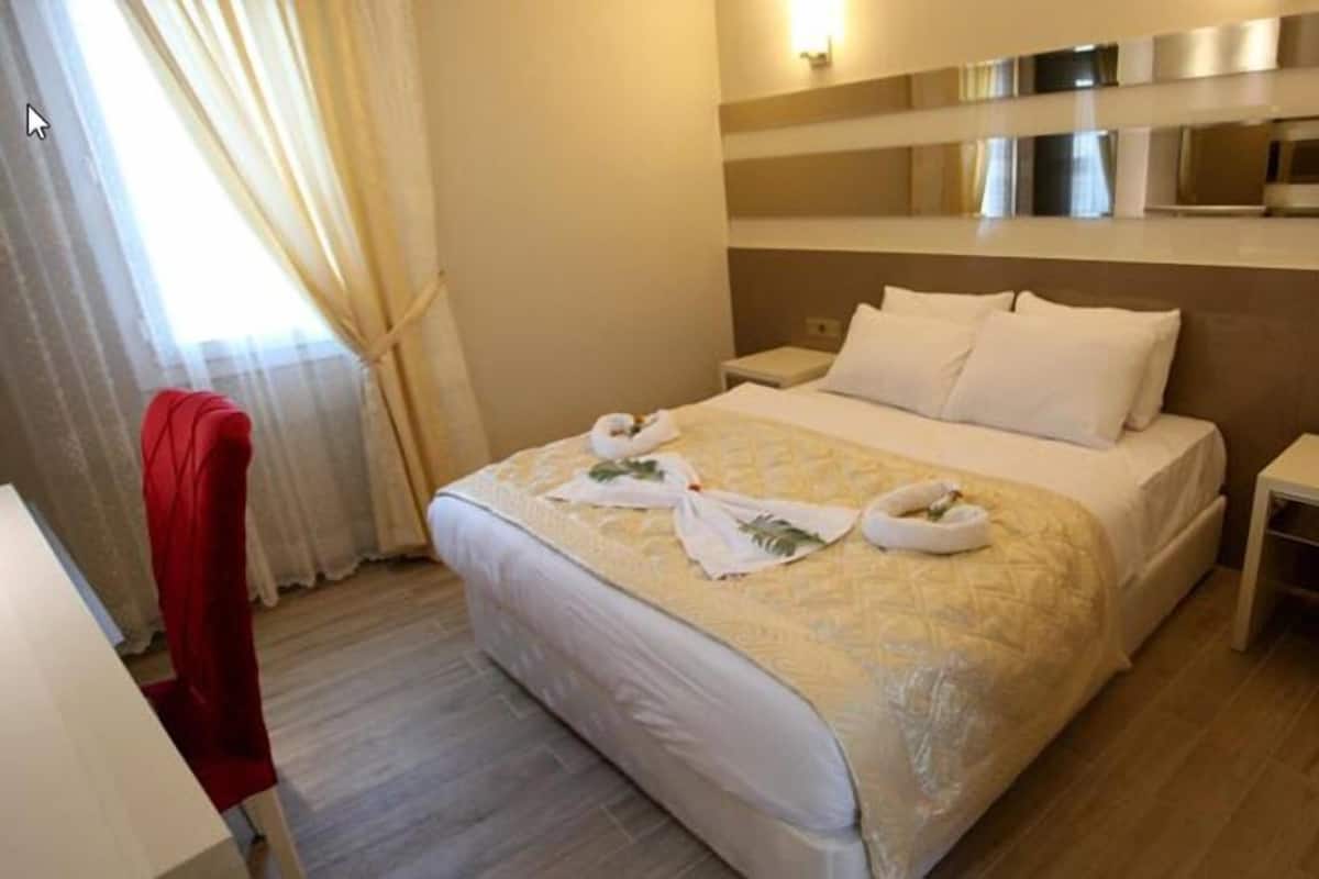 A hotel room with a bed, a bedside table, a red chair, and a window with curtains.