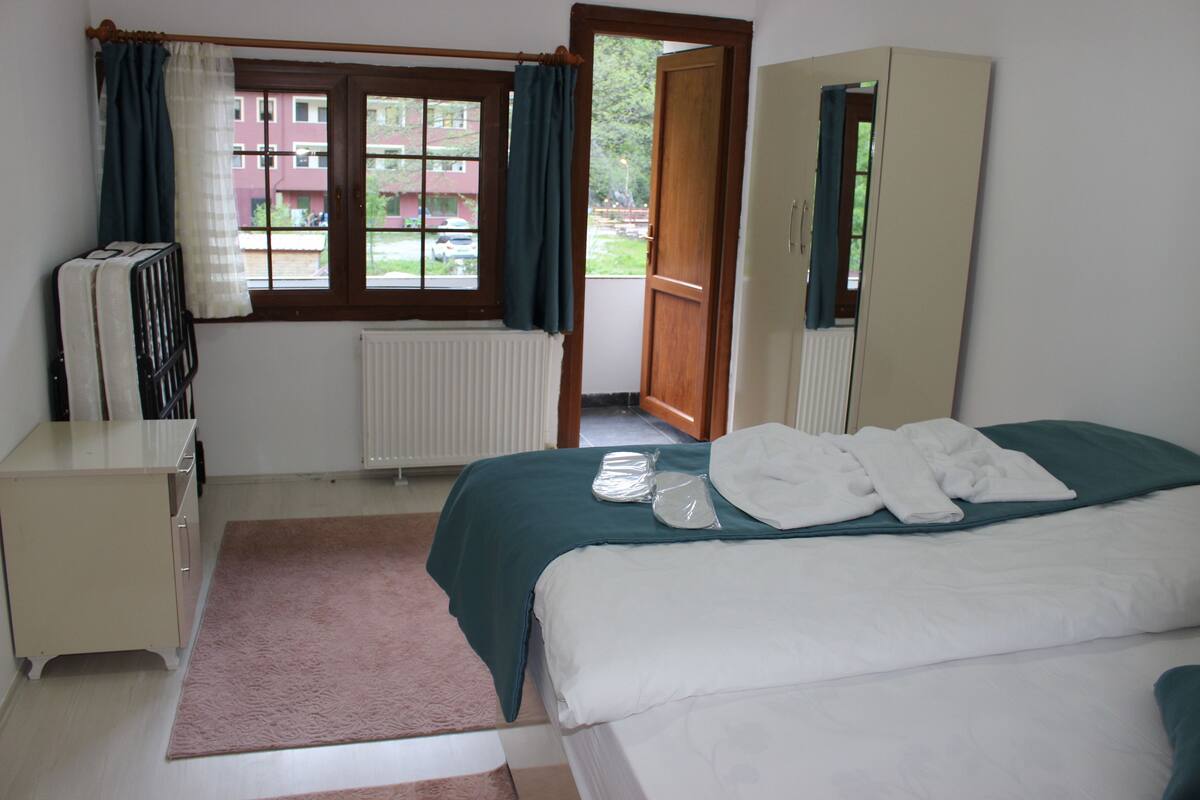 A bedroom with a bed, a dresser, a radiator, a window with curtains, and a door leading to a balcony.