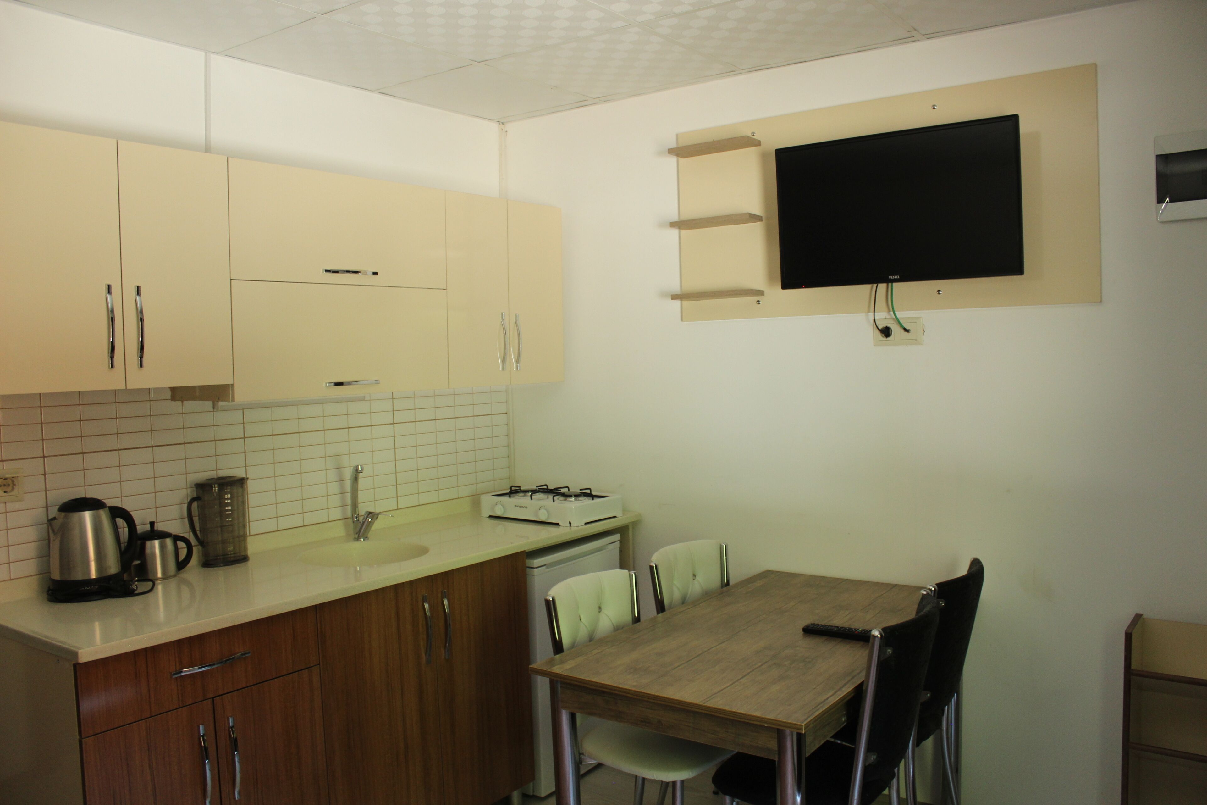 Une cuisine compacte avec des meubles en bois, un plan de travail blanc, une cuisinière encastrée et un téléviseur fixé au mur.