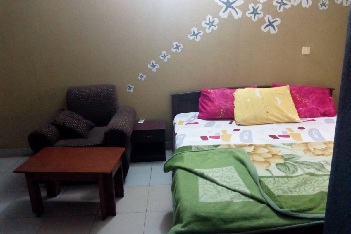 A small, furnished room with a bed, a chair, a table, and a wall decorated with star stickers.