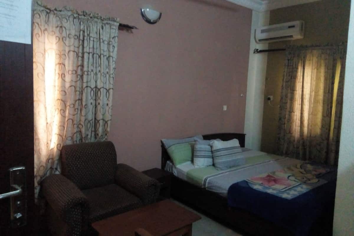 A room with a bed, a sofa, a small table, and an air conditioning unit.