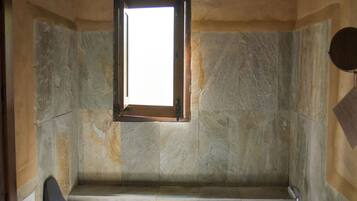 Un baño con pared de piedra, una ventana, una bañera y un taburete de madera.