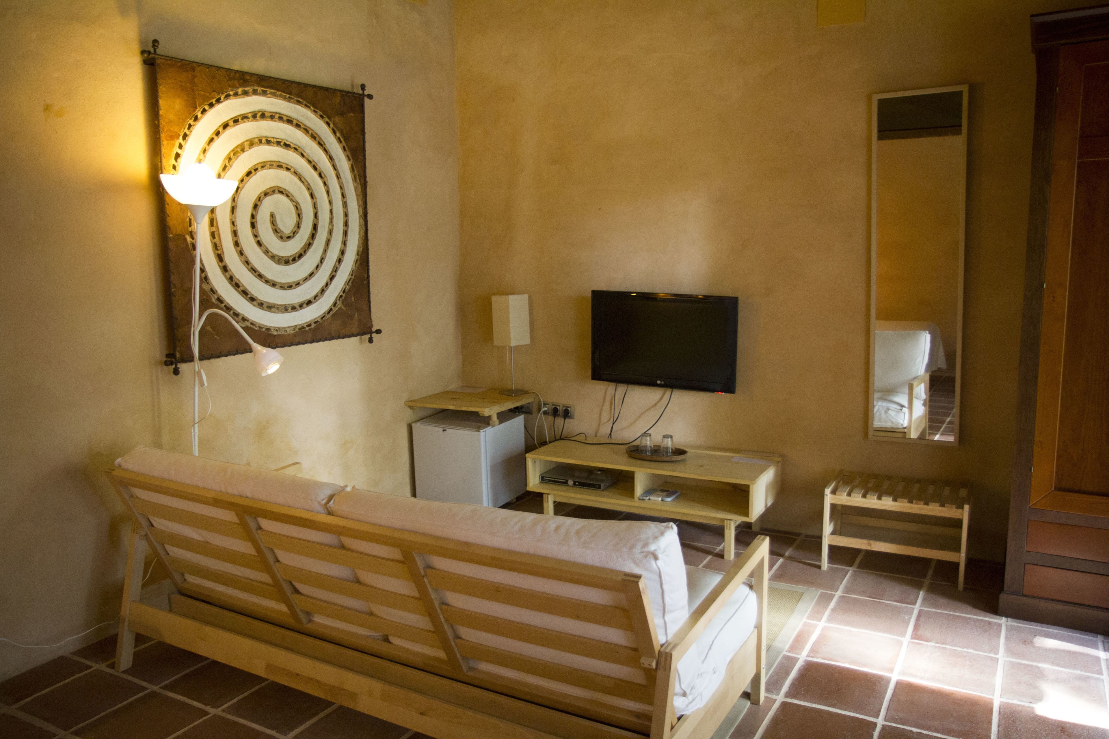 Una habitación pequeña y sencilla con una cama de madera, un televisor, un escritorio pequeño y un espejo.