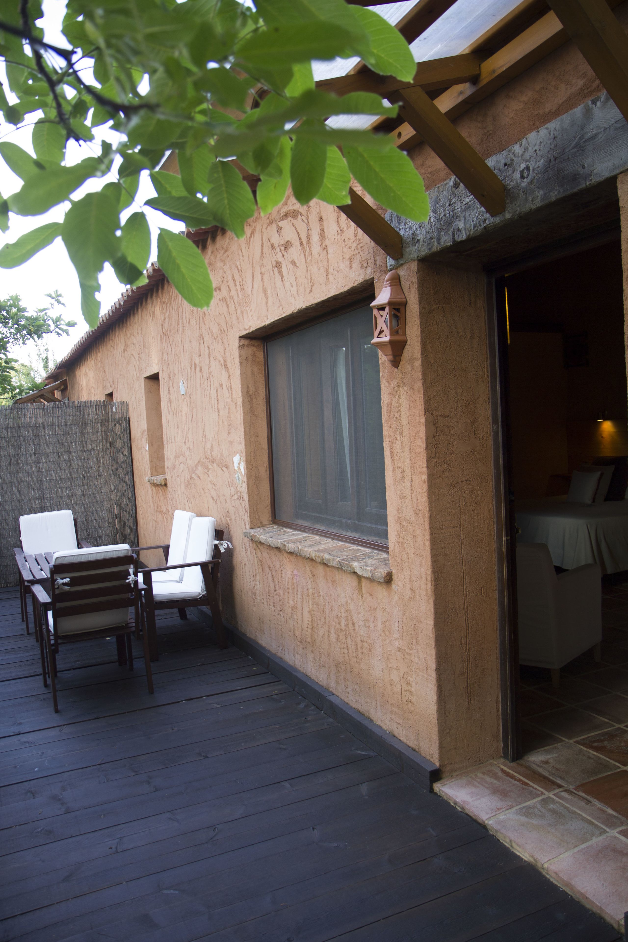 Una terraza de madera con una mesa y sillas, una ventana con cortinas y una puerta que da a una habitación.