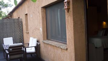 Una terraza de madera con una mesa y sillas, una ventana con cortinas y una puerta que da a una habitación.
