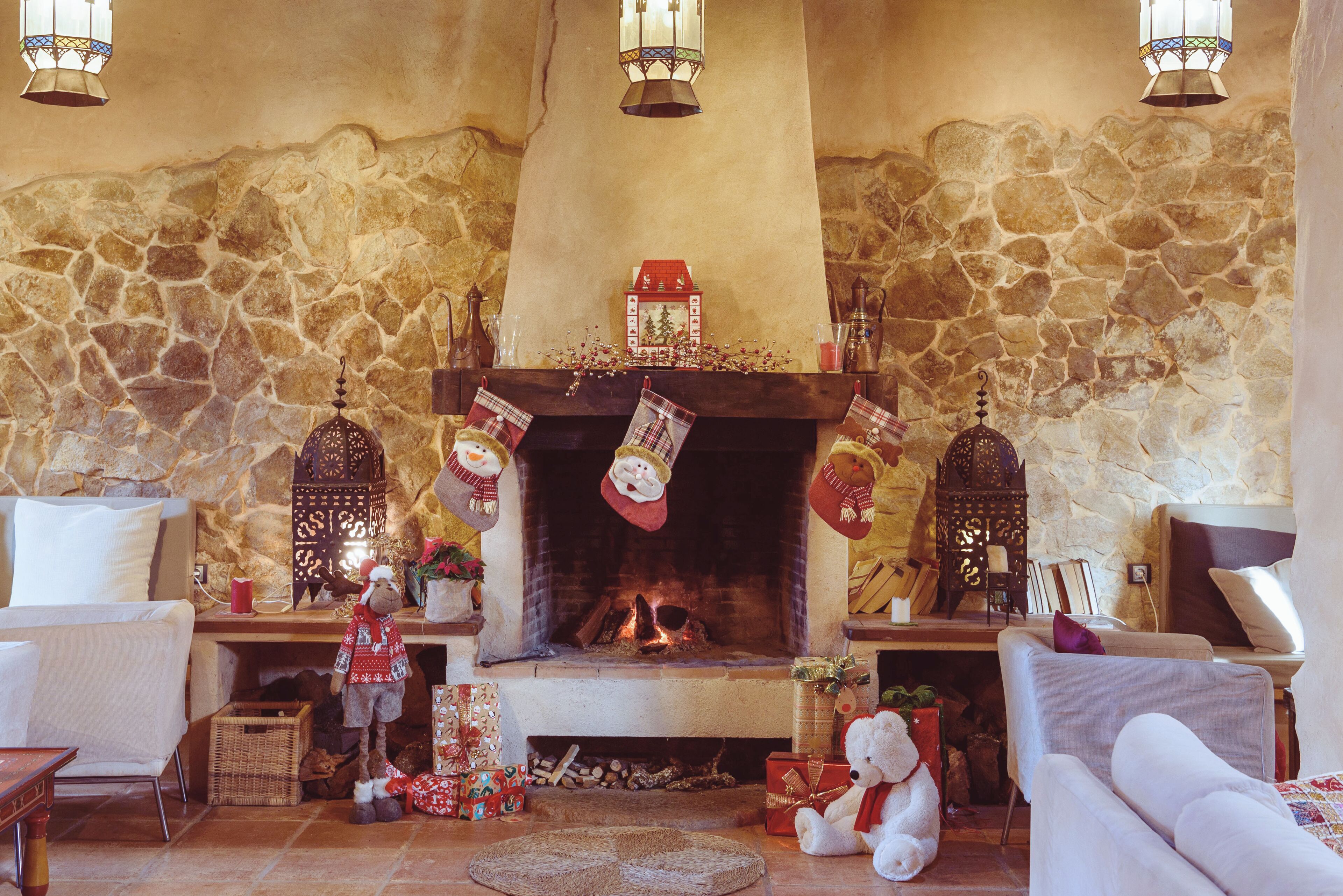 Un salon chaleureux avec une cheminée en pierre, un canapé, une table basse et une étagère de cheminée décorée de chaussettes et d’un petit sapin de Noël.