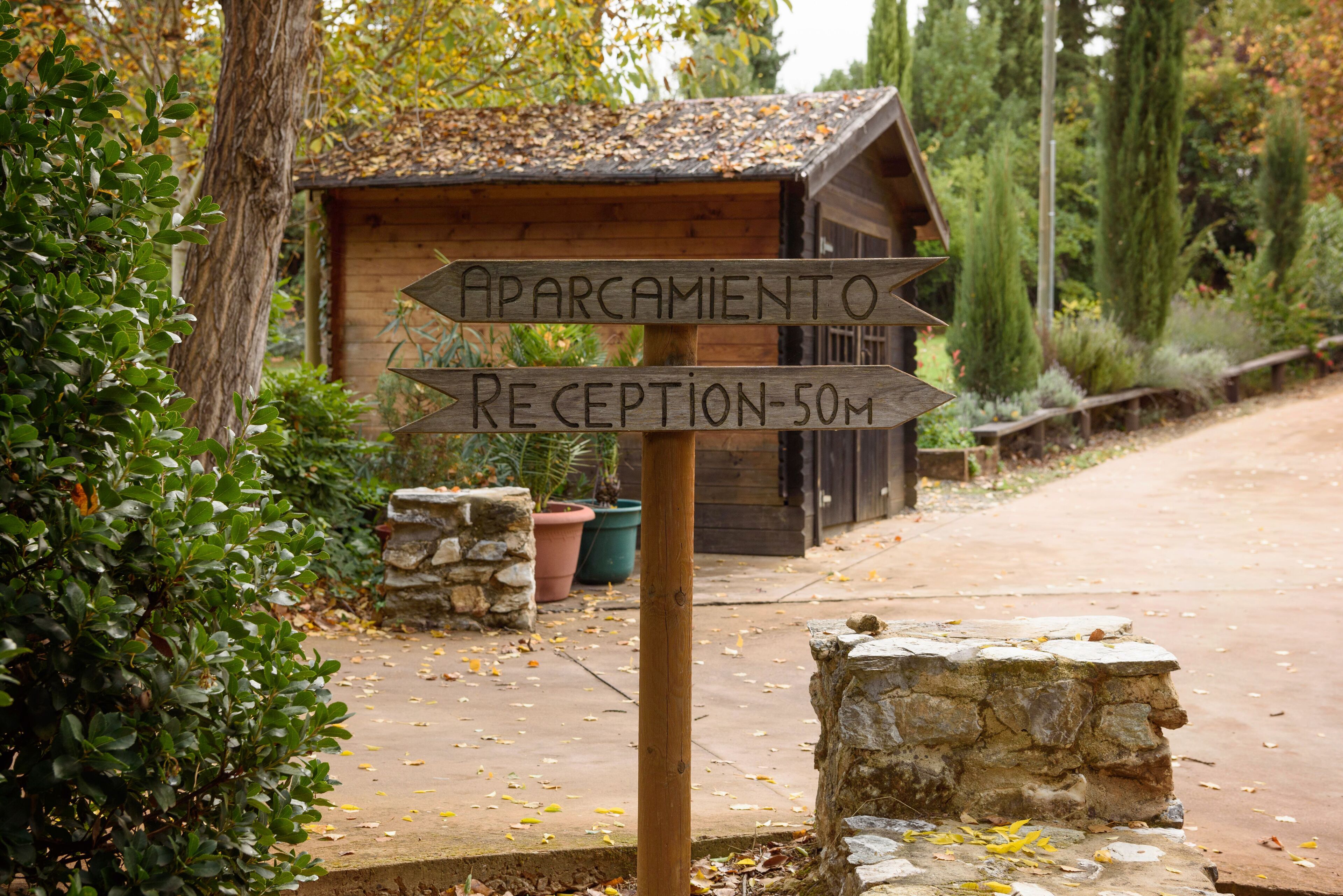 A wooden signpost with directions to 'APARCAMIENTO' and 'RECEPTION-50M'.