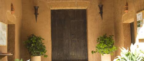Una entrada rústica con puerta de madera, plantas en macetas y suelo de piedra.