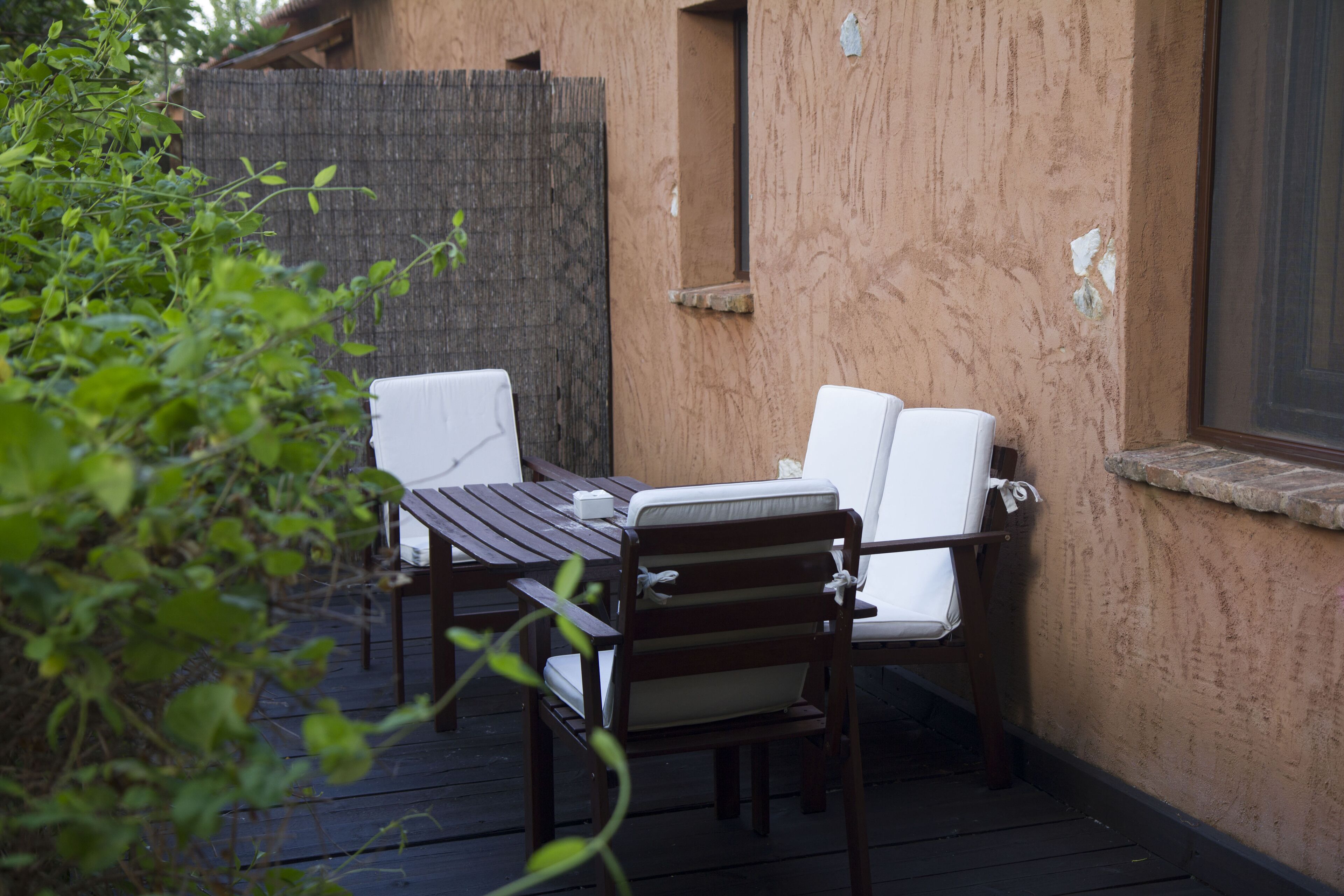 Un patio al aire libre con una mesa de madera y dos sillas blancas con cojines.