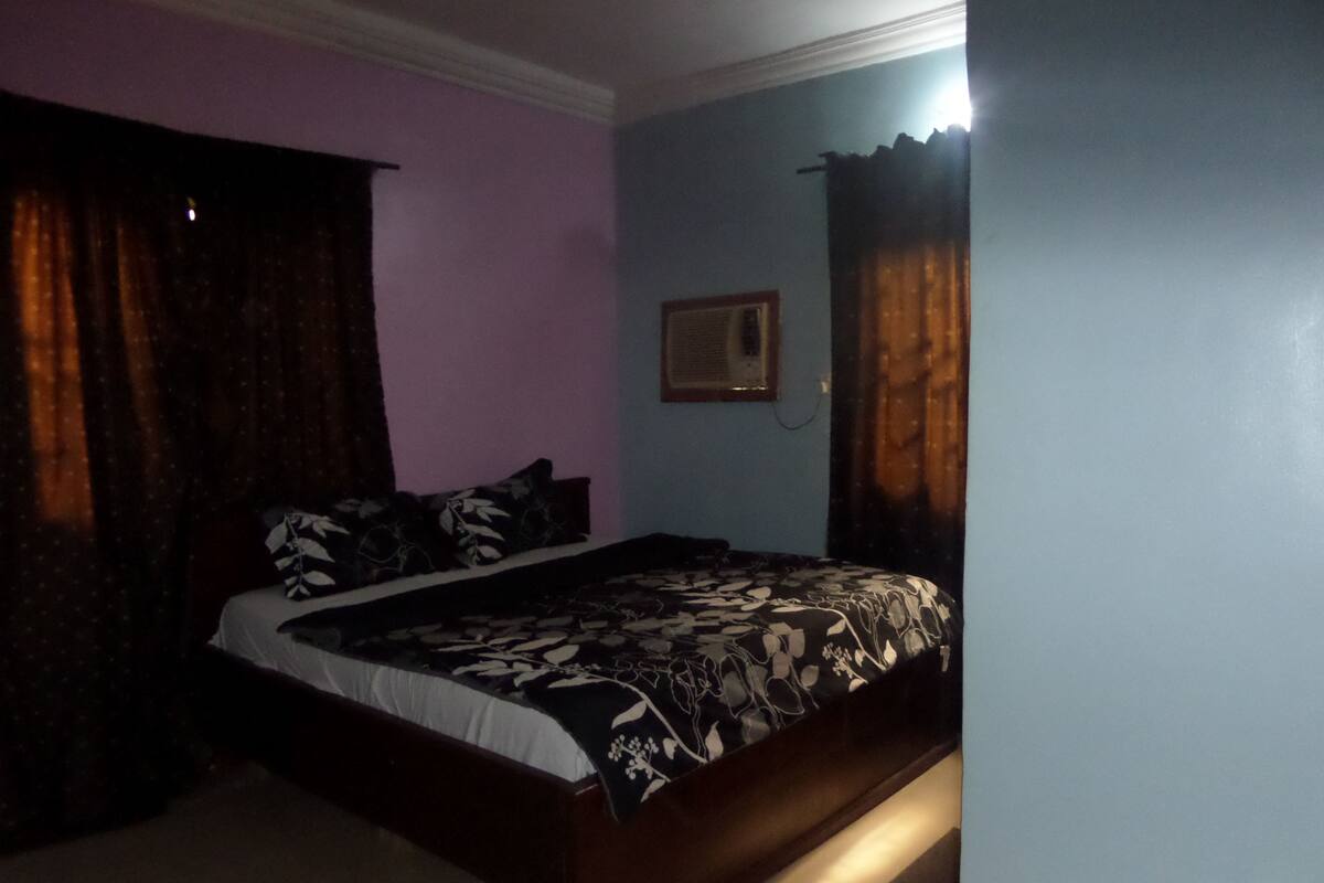 A bedroom with a bed, curtains, and a wall-mounted air conditioner.