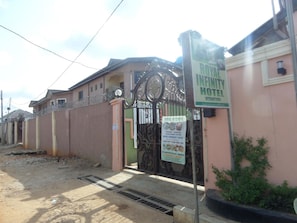 A hotel entrance with a gated driveway, a sign for the Royal Kitchen, and a sign for the Royal Infinity Hotel. - Royal Infinity International Hotel (Lagos)