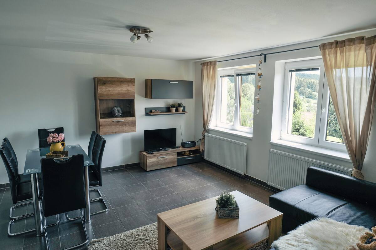 A modern living room with a dining area, a flat-screen TV, and a sofa.