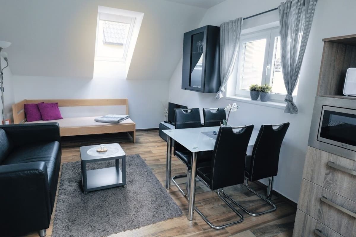 A modern, compact living space with a sofa, a dining table with chairs, a small coffee table, a TV, and a cabinet.
