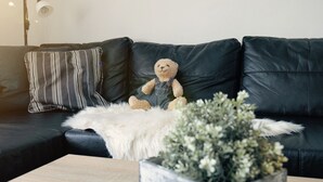 En sort lædersofa med pude med striber, en bamse, et hvidt, blødt tæppe og en potteplante.