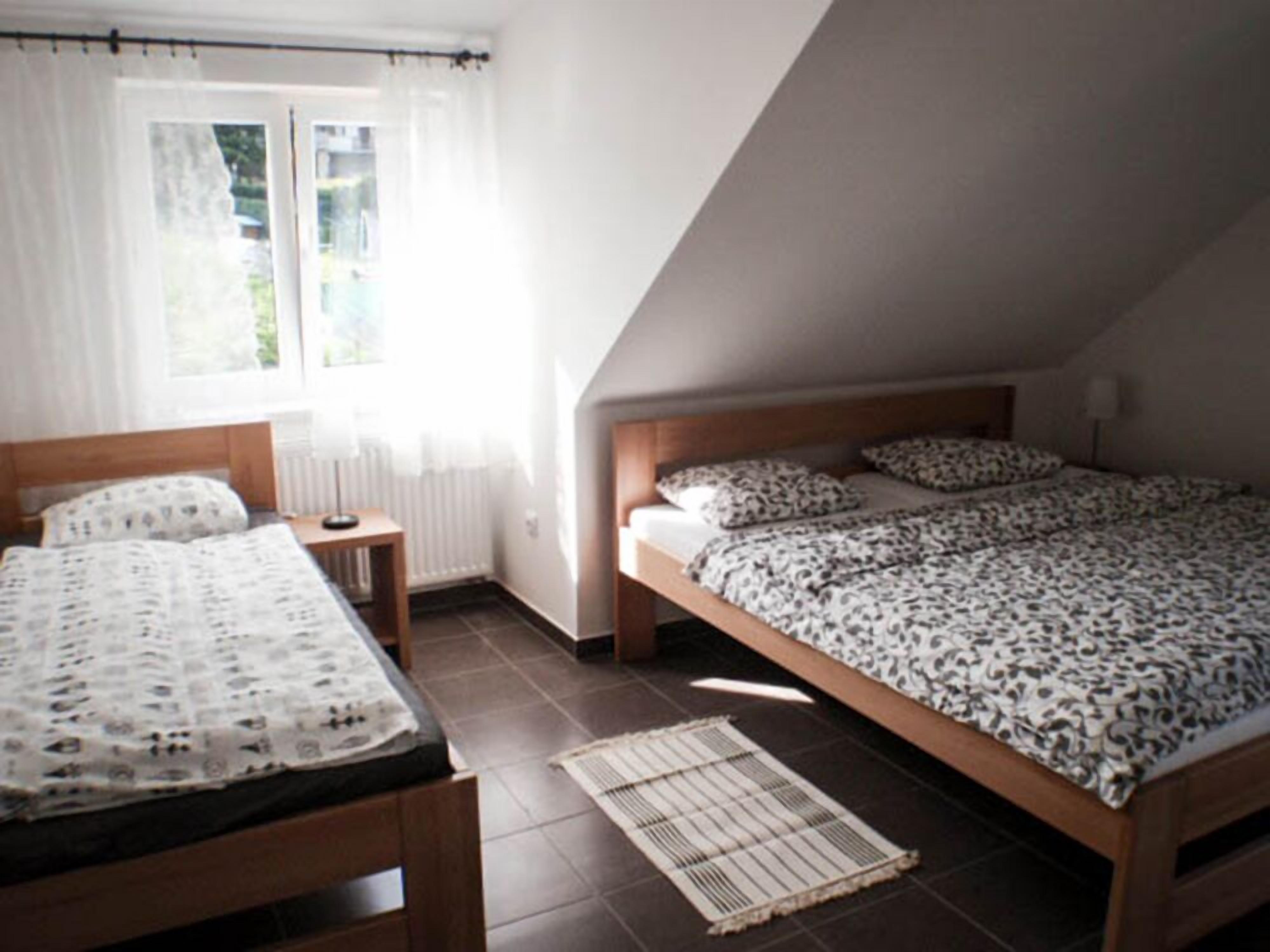 Un dormitorio con techo inclinado, dos camas con ropa de cama estampada, una mesita de noche pequeña y una ventana con cortinas.