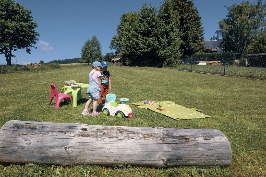 An outdoor area with a grassy field, a wooden log, and children's toys.
