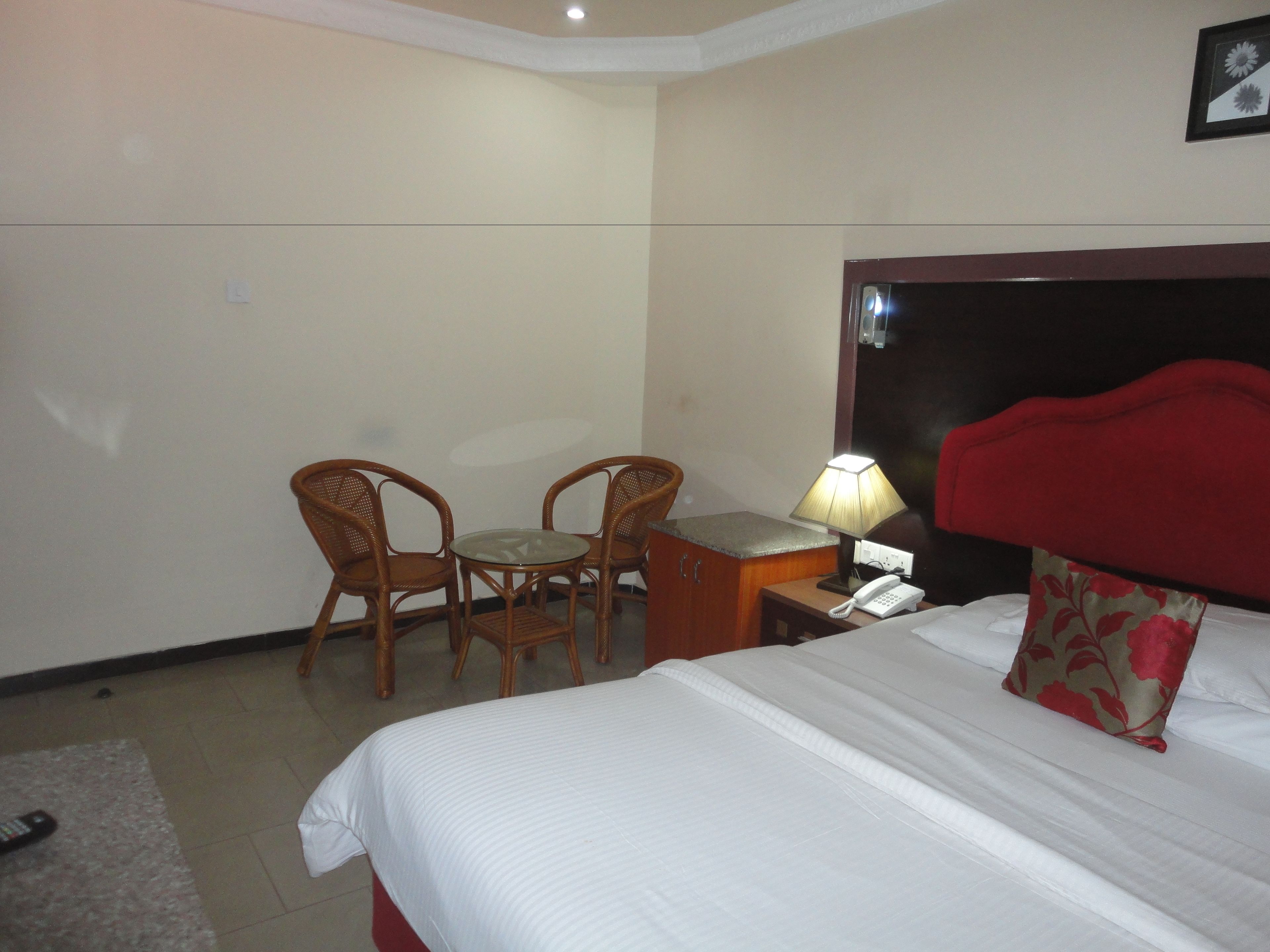 A hotel room with a bed, a desk with a lamp, two chairs, and a telephone.