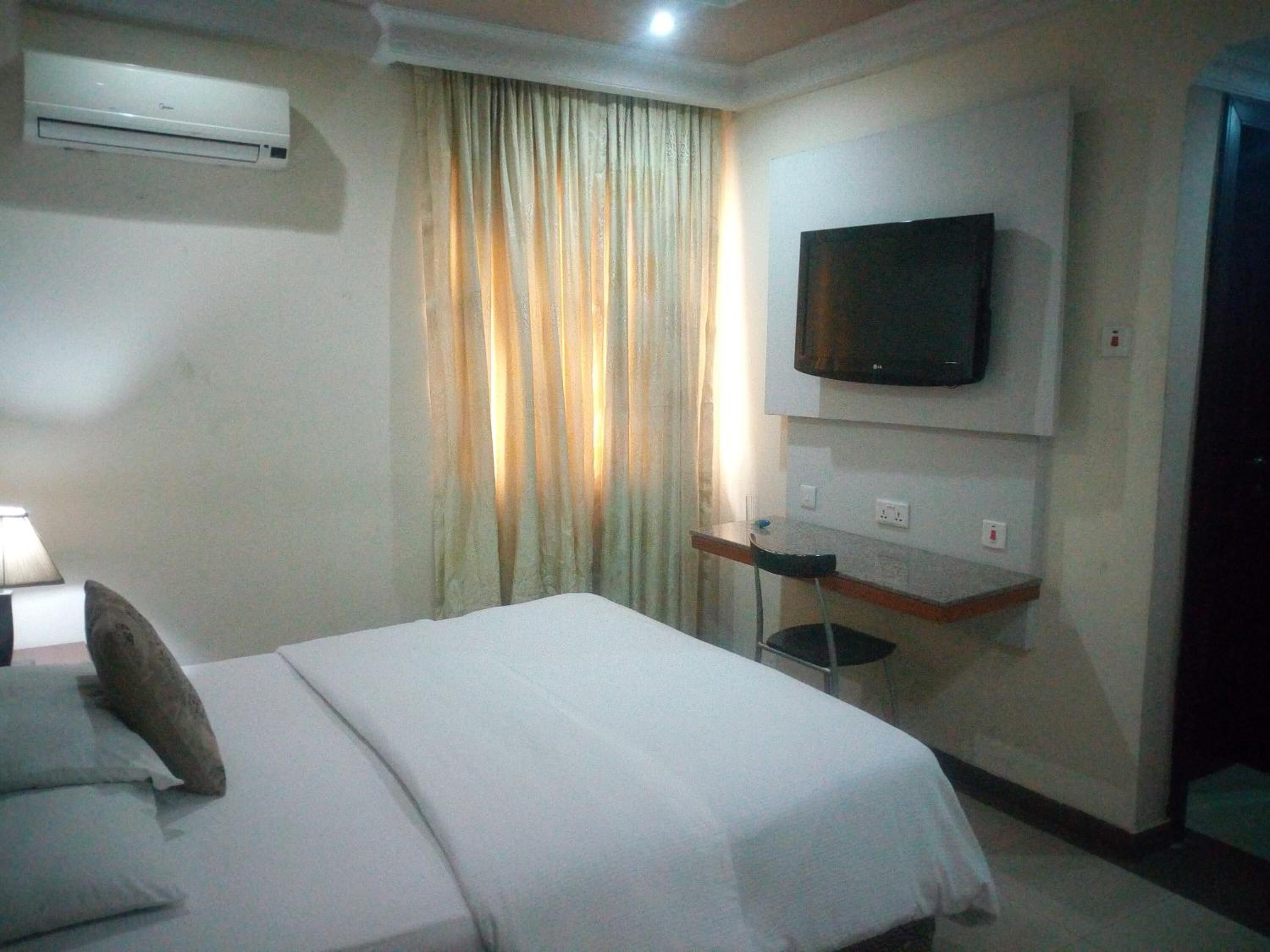 A hotel room with a bed, an air conditioner, a TV mounted on the wall, and a curtain.
