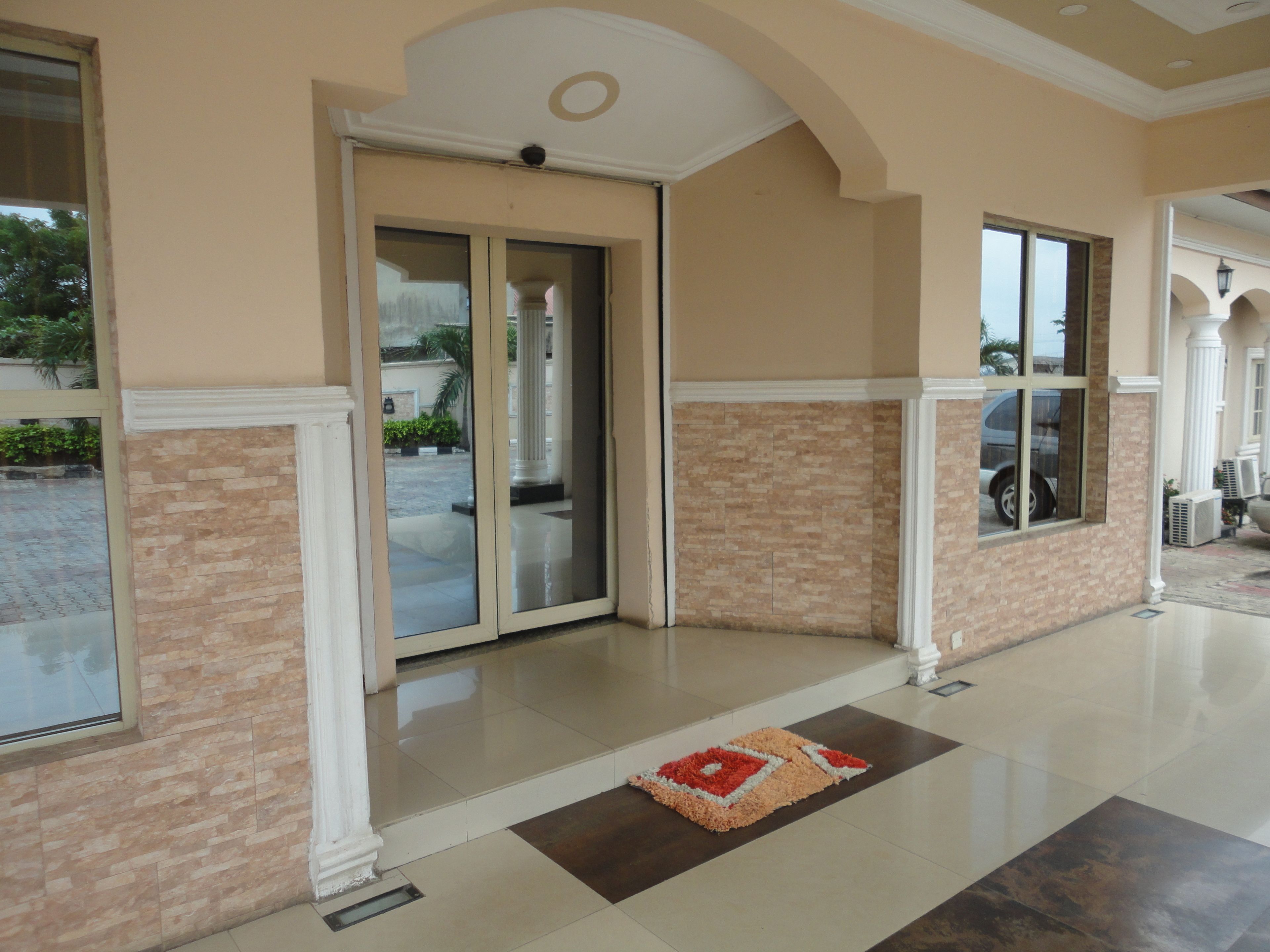 Entrada de hotel con piso de baldosas, alfombra y puerta de cristal que da al estacionamiento.