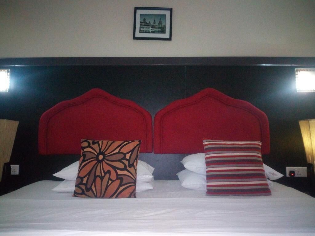 Ein Hotelzimmer mit einem großen Bett, zwei roten Kopfteilen und einem gerahmten Bild an der Wand.